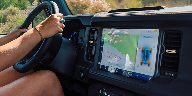 A person driving with their hand on the steering wheel, while the dashboard displays an off-road navigation screen
